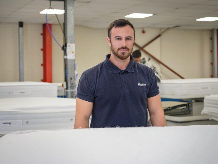 Male employee at the Dreams bed factory smiling at his mattress workstation