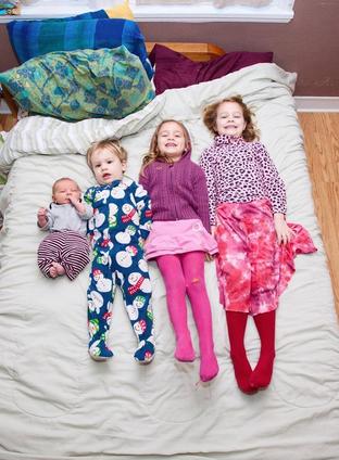Children laying in a row on a bed