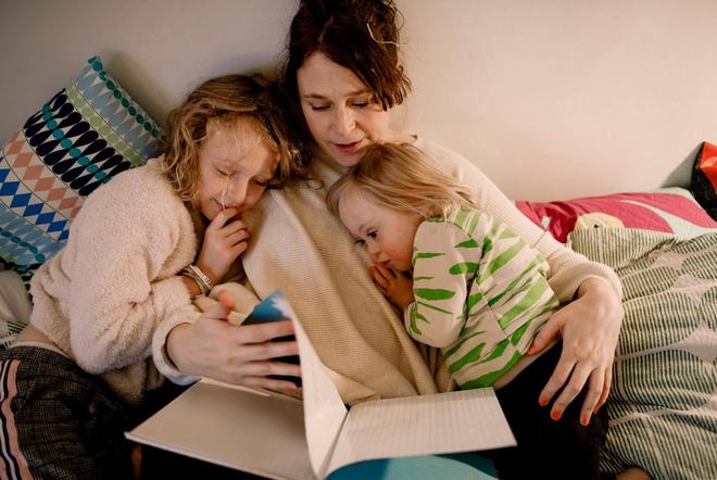 Two children cuddling with their mother reading a book.