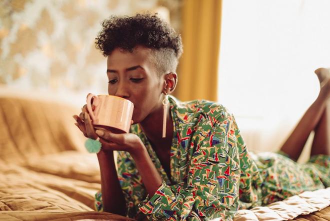 Two people carring a mattress off a Dreavery vanA woman relaxing on her bed drinking a hot drink.