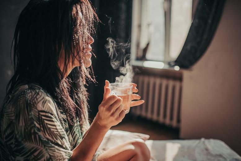 Woman holding mug of tea in bed