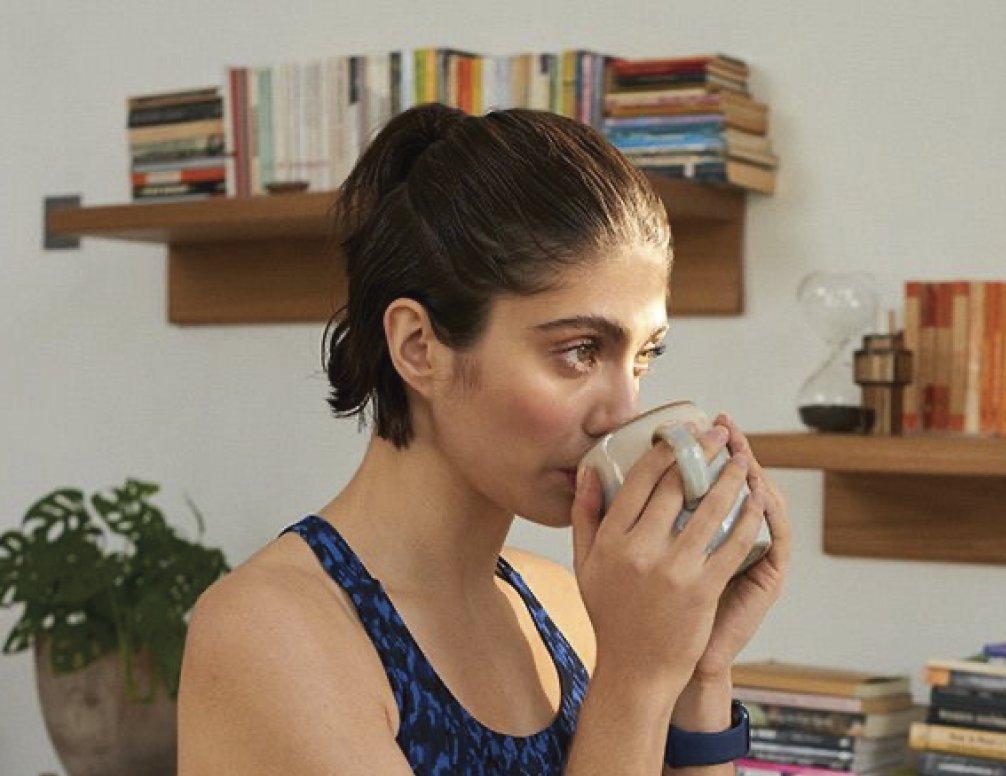 Lady with short hair with her hands clasped around a mug which she has to her mouth