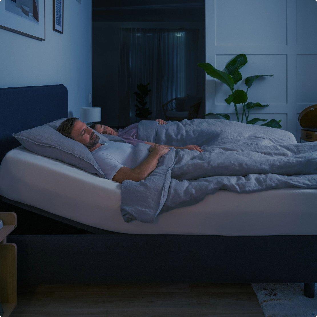 Two people sleeping on a TEMPUR bed, one with raised mattress at head, other person head lowered